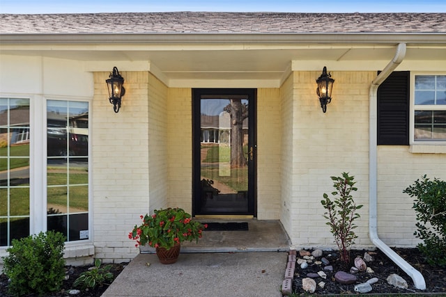entrance to property with roof with shingles and brick siding