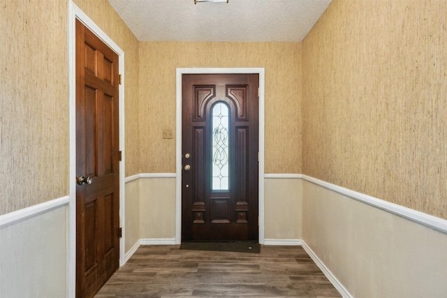 entrance foyer with wallpapered walls, wood finished floors, and a textured ceiling