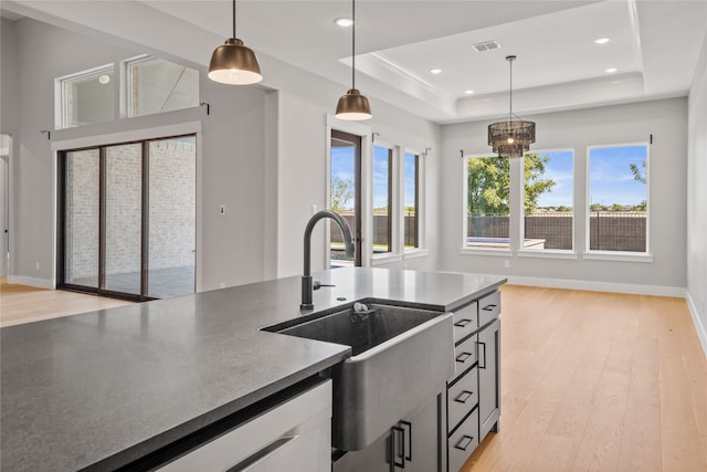 kitchen with pendant lighting, sink, a raised ceiling, and light wood-type flooring