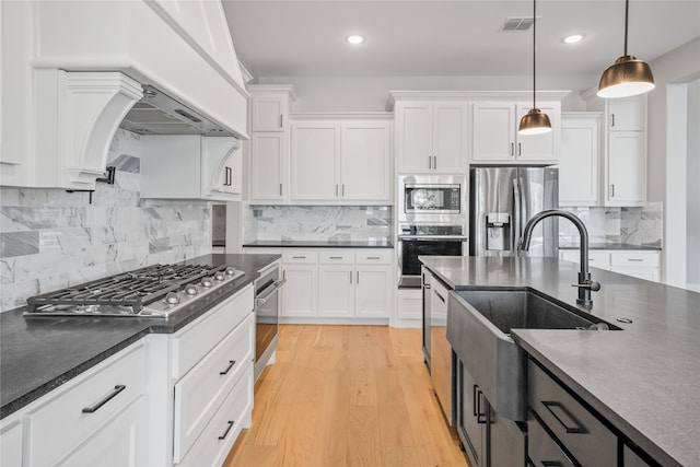 kitchen featuring pendant lighting, sink, appliances with stainless steel finishes, white cabinetry, and light hardwood / wood-style floors