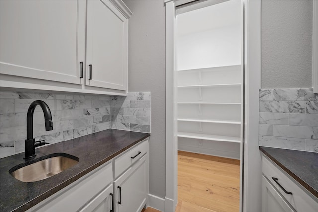 bar featuring white cabinetry, sink, decorative backsplash, dark stone counters, and light hardwood / wood-style flooring