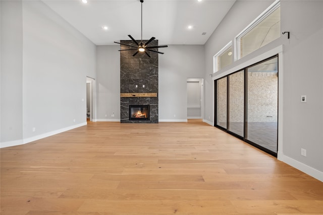 unfurnished living room with light hardwood / wood-style flooring, a towering ceiling, ceiling fan, and a fireplace