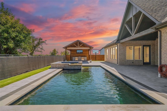 pool at dusk featuring an in ground hot tub and a patio