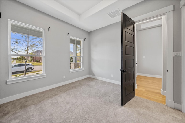 unfurnished bedroom featuring light colored carpet and a tray ceiling