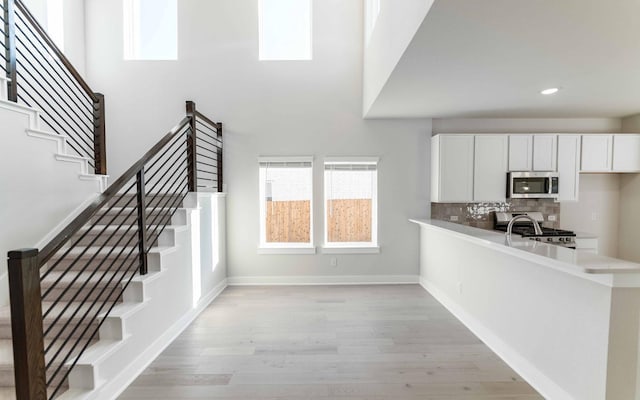 interior space featuring stainless steel appliances, light hardwood / wood-style flooring, backsplash, kitchen peninsula, and white cabinets