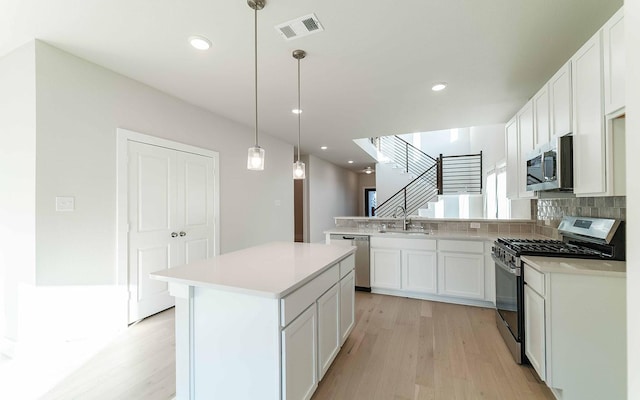 kitchen with white cabinets, stainless steel appliances, decorative light fixtures, and a kitchen island