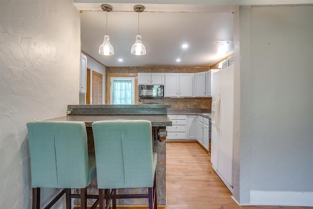 kitchen featuring white refrigerator with ice dispenser, white cabinetry, kitchen peninsula, a kitchen breakfast bar, and light hardwood / wood-style flooring