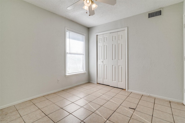 unfurnished bedroom featuring ceiling fan, a closet, light tile patterned flooring, and a textured ceiling