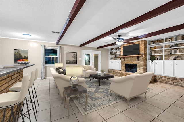 tiled living room featuring ceiling fan, a brick fireplace, built in features, beamed ceiling, and a textured ceiling