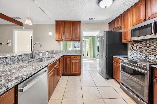 kitchen featuring hanging light fixtures, sink, light stone countertops, appliances with stainless steel finishes, and tasteful backsplash