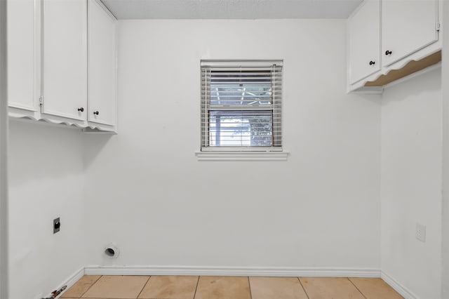 washroom with electric dryer hookup, cabinets, and light tile patterned floors