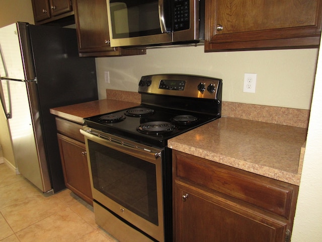 kitchen with light tile patterned flooring, dark brown cabinets, and stainless steel appliances