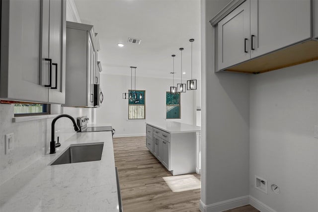 kitchen with gray cabinets, light wood-type flooring, sink, hanging light fixtures, and appliances with stainless steel finishes