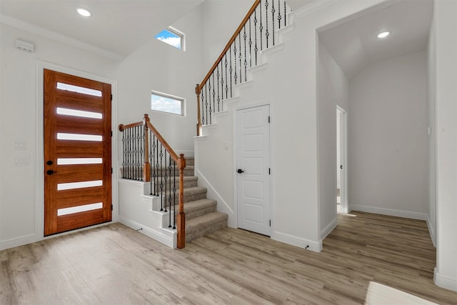 foyer featuring light hardwood / wood-style flooring, a towering ceiling, and crown molding