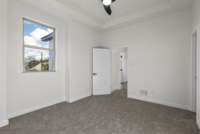 unfurnished bedroom with a tray ceiling, dark carpet, and ceiling fan