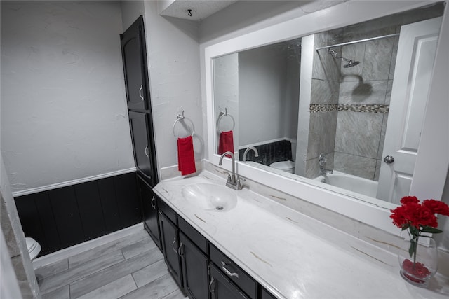 full bathroom featuring hardwood / wood-style floors, tiled shower / bath combo, vanity, and toilet