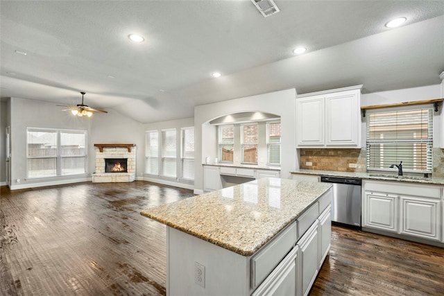 kitchen featuring visible vents, a sink, stainless steel dishwasher, a fireplace, and vaulted ceiling