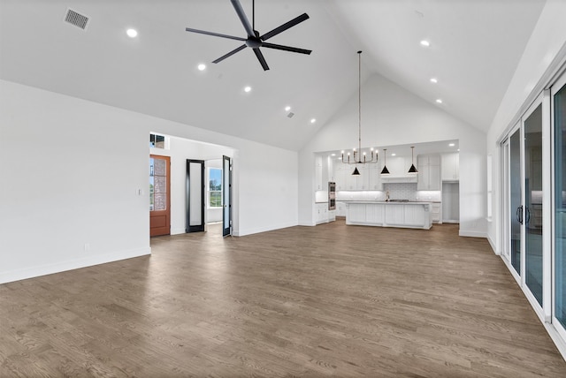 unfurnished living room featuring ceiling fan with notable chandelier, dark hardwood / wood-style floors, sink, and high vaulted ceiling