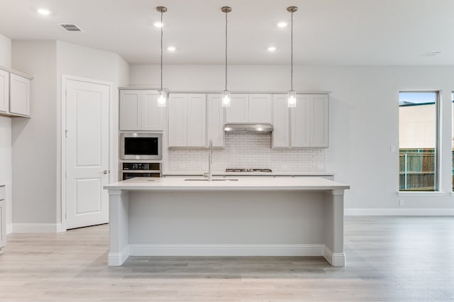 kitchen featuring sink, light hardwood / wood-style floors, hanging light fixtures, and a kitchen island with sink