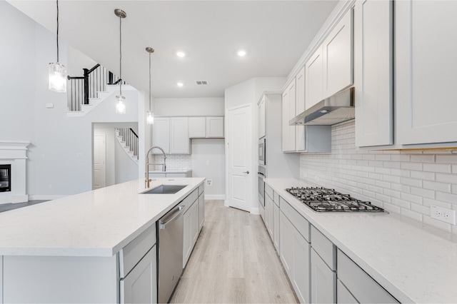 kitchen featuring appliances with stainless steel finishes, light wood-type flooring, extractor fan, sink, and an island with sink