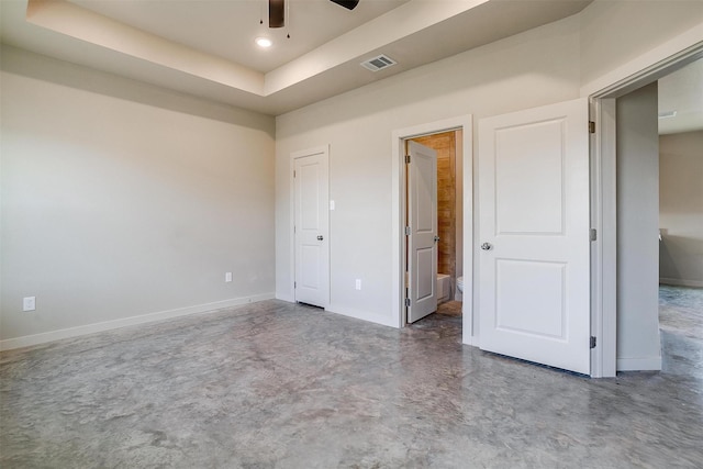 unfurnished bedroom featuring ceiling fan, connected bathroom, a tray ceiling, and concrete floors