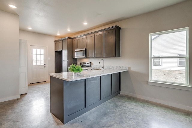 kitchen featuring kitchen peninsula, sink, light stone countertops, stainless steel appliances, and dark brown cabinets