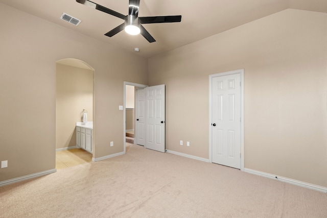 unfurnished bedroom featuring lofted ceiling, ensuite bathroom, ceiling fan, and light colored carpet