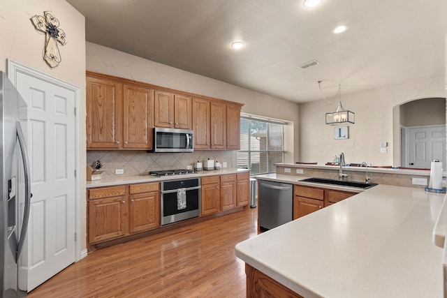 kitchen with sink, pendant lighting, light wood-type flooring, and appliances with stainless steel finishes