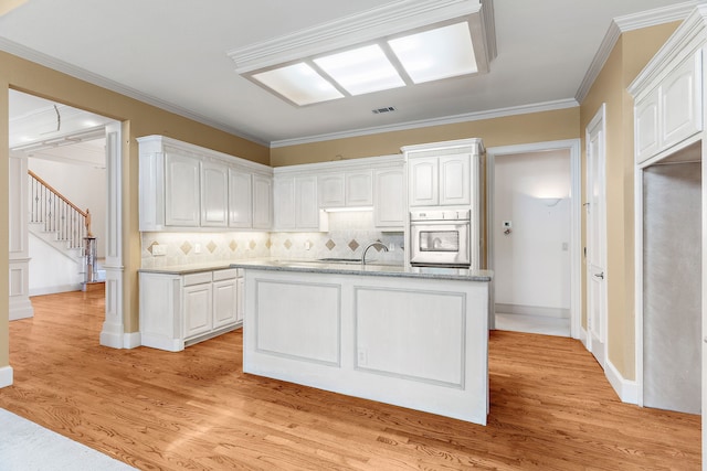 kitchen featuring oven, white cabinets, decorative backsplash, light hardwood / wood-style flooring, and ornamental molding