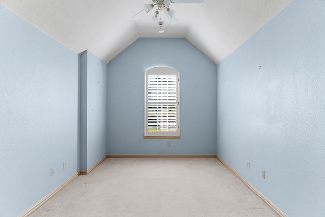 empty room featuring a textured ceiling, vaulted ceiling, light colored carpet, and ceiling fan