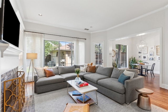 living room with an inviting chandelier, a tile fireplace, ornamental molding, and hardwood / wood-style floors