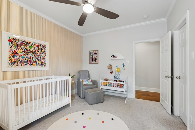 bedroom with a crib, light colored carpet, crown molding, and ceiling fan