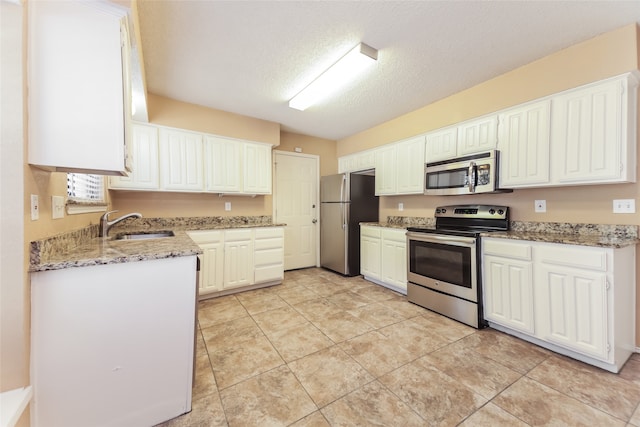 kitchen with light stone counters, white cabinets, light tile patterned floors, stainless steel appliances, and a textured ceiling