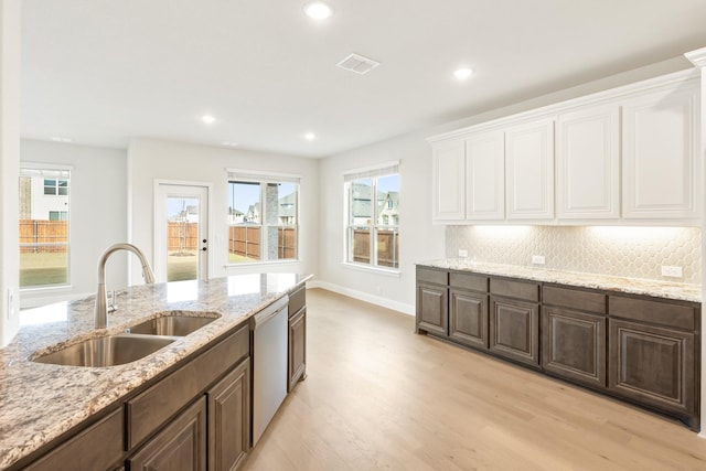 kitchen with sink, light hardwood / wood-style flooring, stainless steel dishwasher, light stone countertops, and white cabinetry