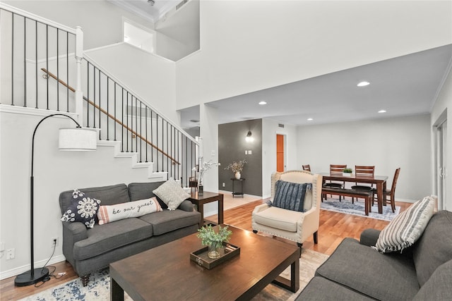 living room with light wood-type flooring, a towering ceiling, and crown molding