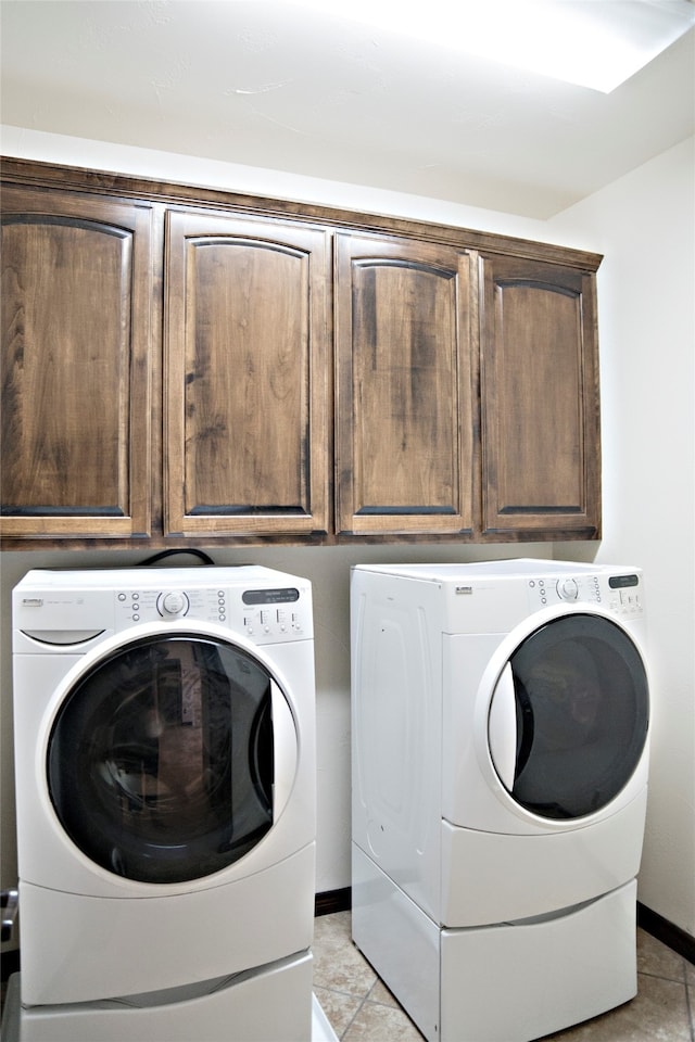 clothes washing area with cabinets, light tile patterned flooring, and washer and clothes dryer