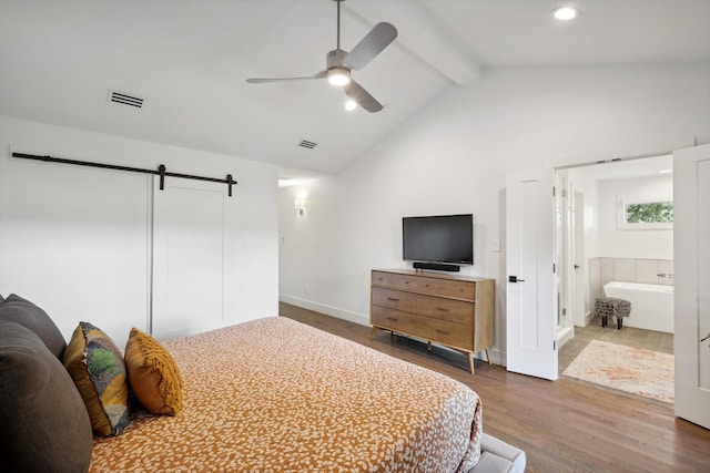 bedroom featuring lofted ceiling with beams, a barn door, connected bathroom, hardwood / wood-style floors, and ceiling fan