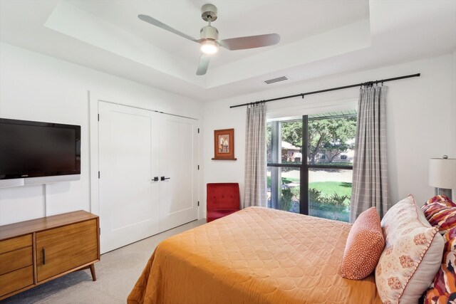 bedroom with a closet, light colored carpet, ceiling fan, and a raised ceiling