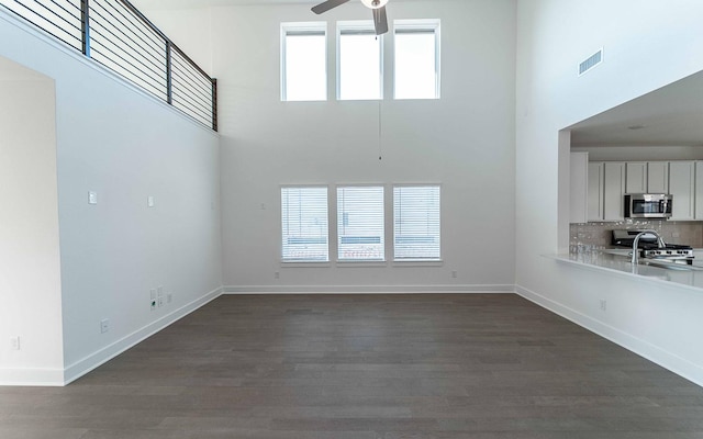 unfurnished living room featuring ceiling fan, dark hardwood / wood-style floors, and a towering ceiling