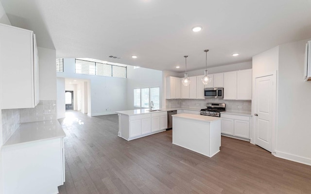 kitchen featuring kitchen peninsula, pendant lighting, stainless steel appliances, and white cabinetry