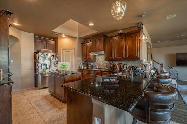 kitchen with stainless steel fridge with ice dispenser, sink, a kitchen island, decorative backsplash, and dark stone countertops