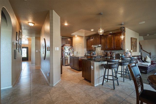 kitchen featuring pendant lighting, a textured ceiling, stainless steel refrigerator with ice dispenser, a breakfast bar area, and decorative backsplash