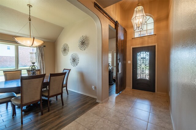 foyer with a barn door, wood-type flooring, lofted ceiling, and an inviting chandelier