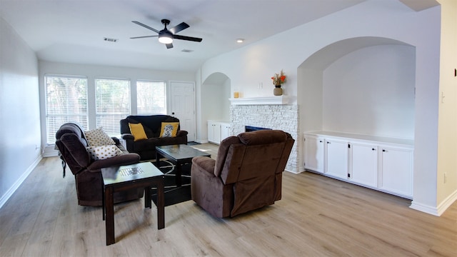 living room with ceiling fan, a stone fireplace, light hardwood / wood-style flooring, and lofted ceiling