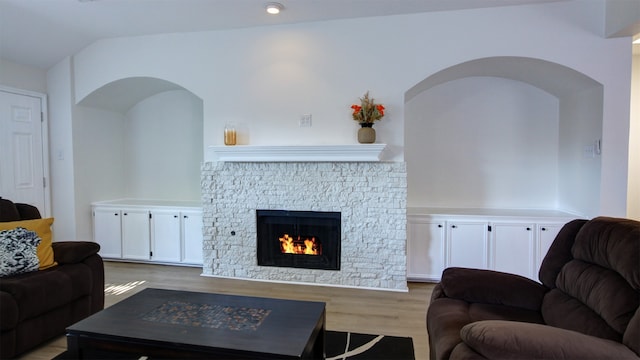 living room with light wood-type flooring, vaulted ceiling, and a fireplace