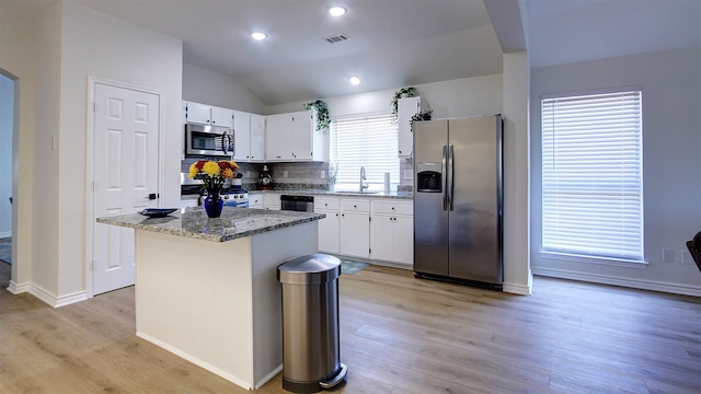 kitchen with lofted ceiling, sink, a kitchen island, appliances with stainless steel finishes, and light stone countertops