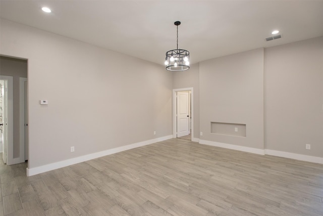 spare room with a notable chandelier and light hardwood / wood-style flooring