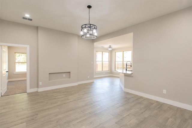 unfurnished living room featuring light hardwood / wood-style flooring, a chandelier, and sink