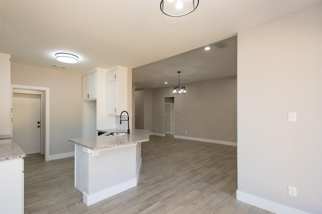 kitchen featuring light stone countertops, light hardwood / wood-style flooring, white cabinets, and hanging light fixtures