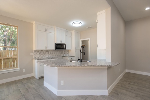 kitchen with sink, light hardwood / wood-style flooring, white cabinetry, light stone counters, and kitchen peninsula